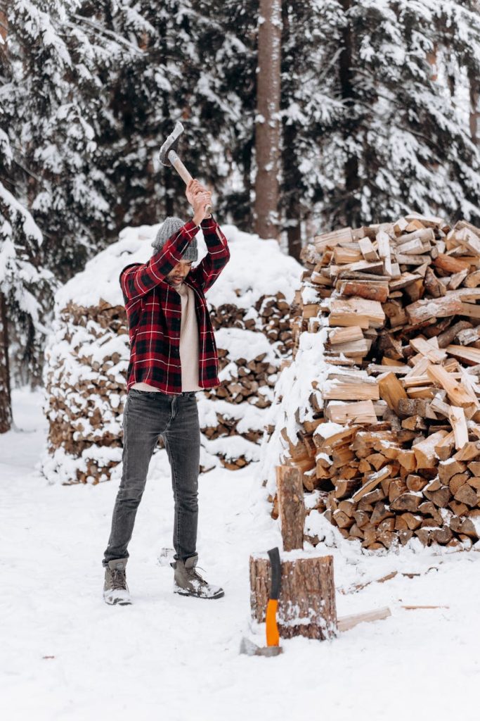 Man chopping wood in snowy forest, winter preparation.