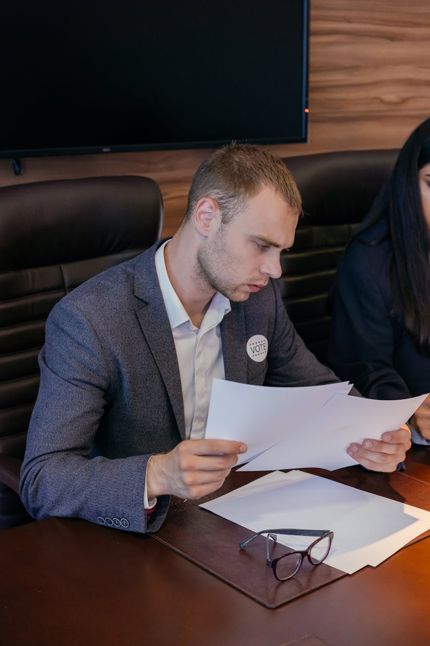 A focused young man reviews political documents in an office setting, planning strategy.