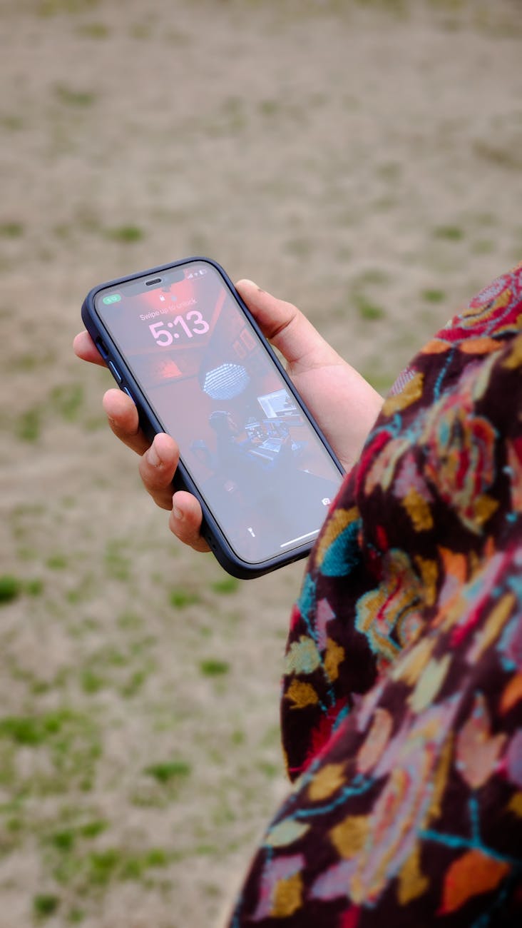 A person holds a smartphone outdoors, displaying a colorful scarf and dynamic phone screen.